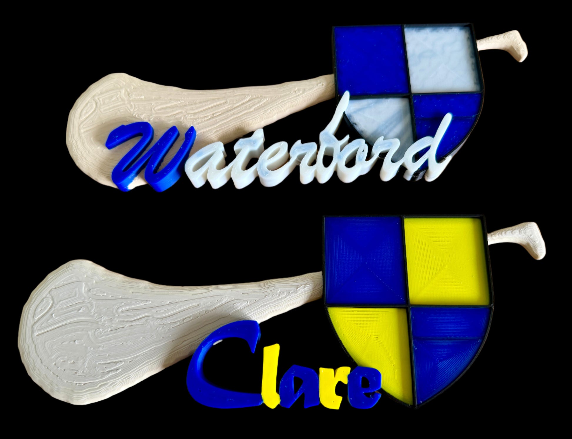 Custom hurley name plates with 'Waterford' and 'Clare' text, featuring a wood-textured handle and patchwork blade in red, blue, and grey. Perfect for hurling and camogie fans.